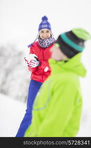 Smiling young woman having snowball fight with male friend