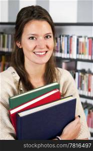 Smiling young woman holding a stack of colorful hardcover books in a library