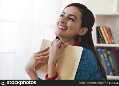 Smiling young woman holding book in living room