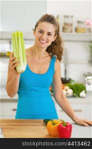 Smiling young woman holding celery in modern kitchen