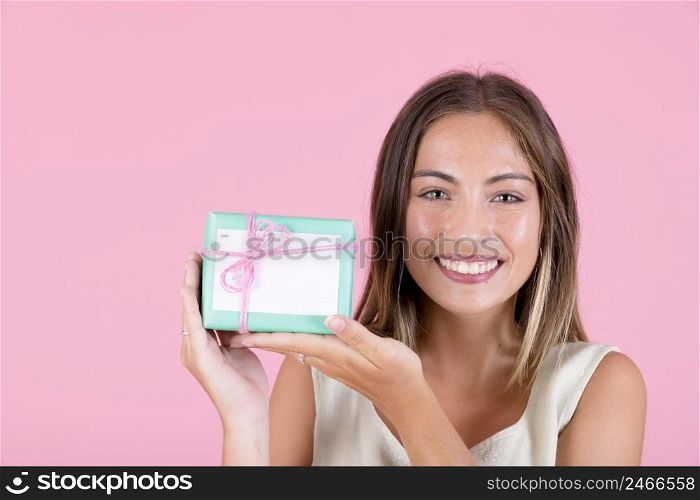 smiling young woman holding gift box tied with pink string