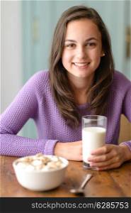 Smiling young woman holding glass of milk cereal breakfast table