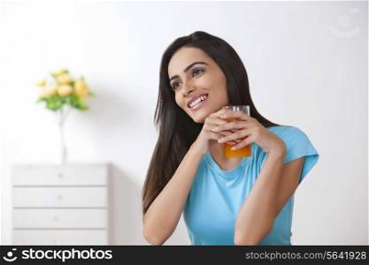 Smiling young woman holding glass of orange juice at home
