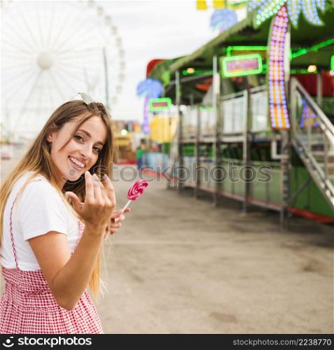 smiling young woman holding lollipop inviting someone come amusement park