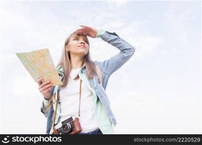 smiling young woman holding map hand shielding her eyes