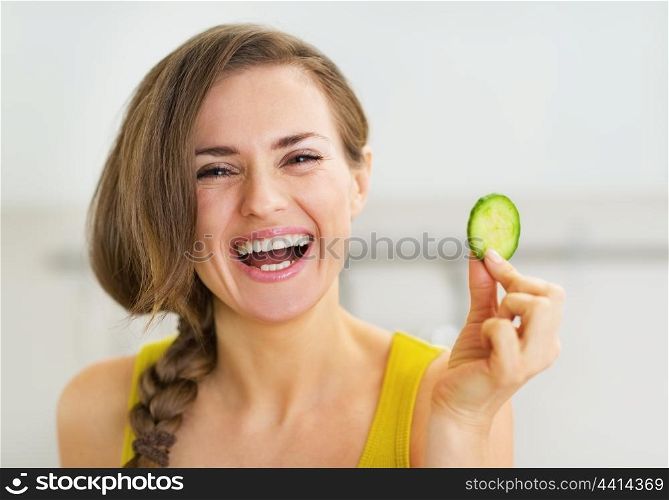 Smiling young woman holding slice of cucumber