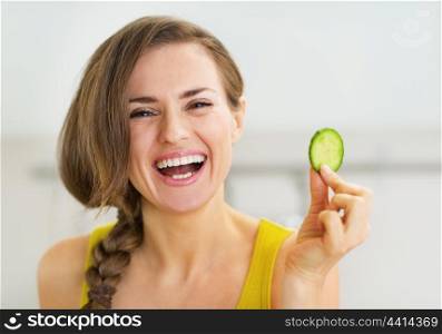Smiling young woman holding slice of cucumber