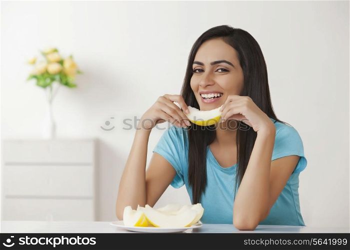 Smiling young woman holding slice of melon at home