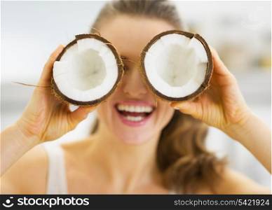 Smiling young woman holding two pieces of coconut in front of eyes