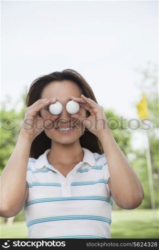 Smiling young woman holding up golf balls in front of her eyes