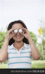 Smiling young woman holding up golf balls in front of her eyes