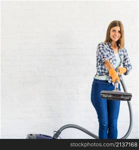 smiling young woman holding vacuum cleaner front brick wall