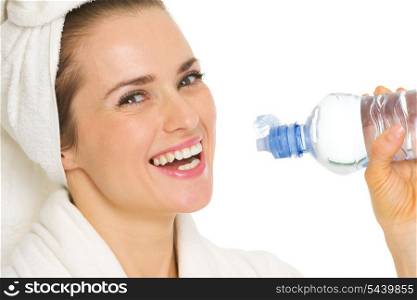 Smiling young woman in bathrobe drinking water from bottle