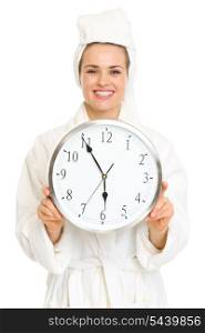 Smiling young woman in bathrobe holding clock