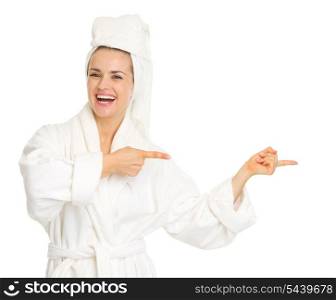 Smiling young woman in bathrobe pointing on copy space