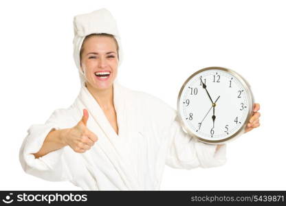 Smiling young woman in bathrobe showing clock and thumbs up