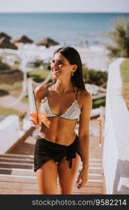 Smiling Young Woman in Bikini Enjoying Vacation on the Beach while drinking cocktail