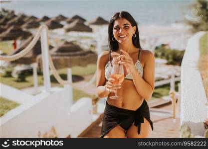 Smiling Young Woman in Bikini Enjoying Vacation on the Beach while drinking cocktail