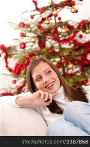 Smiling young woman in front of Christmas tree sitting