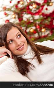 Smiling young woman in front of Christmas tree sitting