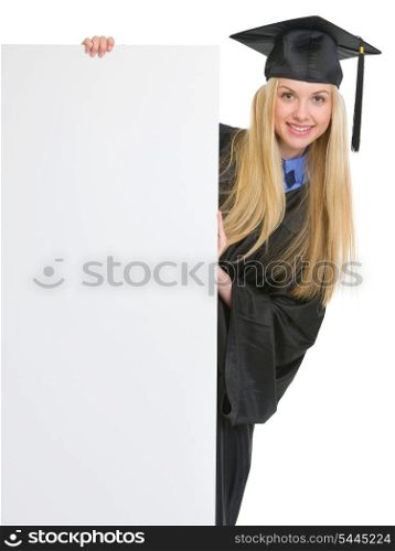 Smiling young woman in graduation gown looking out from blank billboard
