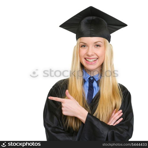 Smiling young woman in graduation gown pointing on copy space