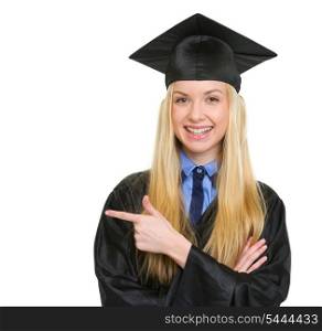 Smiling young woman in graduation gown pointing on copy space