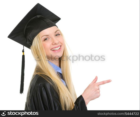 Smiling young woman in graduation gown pointing on copy space