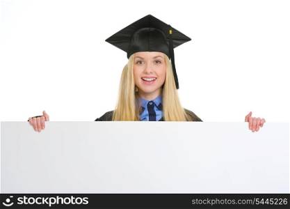 Smiling young woman in graduation gown showing blank billboard