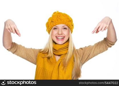 Smiling young woman in hat and scarf pointing down on copy space