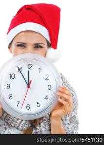 Smiling young woman in sweater and christmas hat hiding behind clock