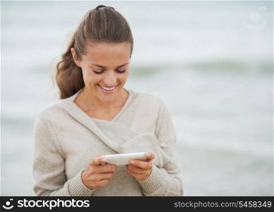 Smiling young woman in sweater on beach writing sms