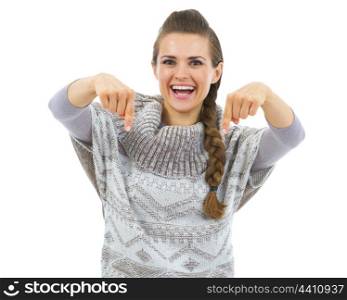 Smiling young woman in sweater pointing down on copy space
