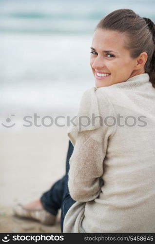 Smiling young woman in sweater sitting on lonely beach