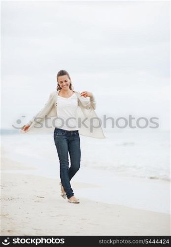 Smiling young woman in sweater walking on lonely beach