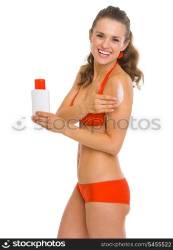 Smiling young woman in swimsuit applying sun screen creme