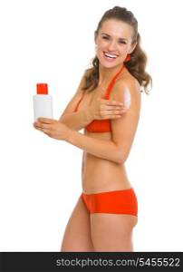 Smiling young woman in swimsuit applying sun screen creme
