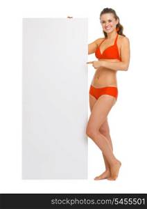 Smiling young woman in swimsuit pointing on blank billboard