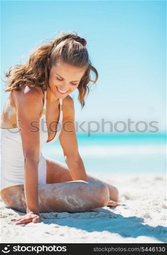 Smiling young woman in swimsuit sitting on sea coast