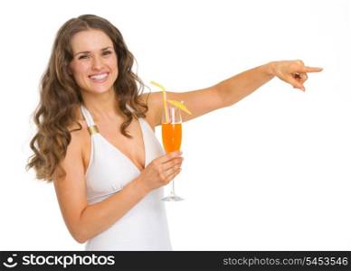 Smiling young woman in swimsuit with cocktail pointing on copy space