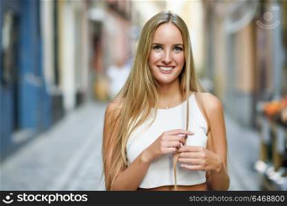 Smiling young woman in urban background. Blond girl wearing with nice hair casual clothes in the street. Straight hairstyle.