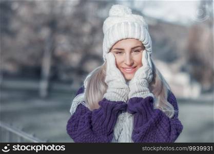 Smiling young woman in warm clothing on winter day outdoors. Happy girl wearing wool cap, scarf and sweater. Snow people concept. Female person in cold weather.