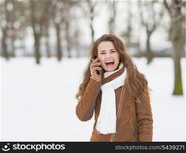 Smiling young woman in winter park talking cell phone