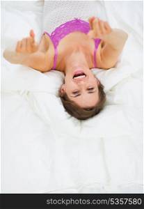 Smiling young woman laying on bed and pointing in camera