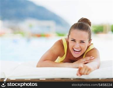 Smiling young woman laying on chaise-longue and pointing in camera