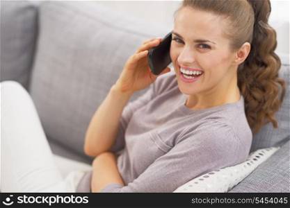 Smiling young woman laying on couch and talking cell phone