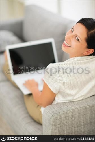 Smiling young woman laying on couch and using laptop