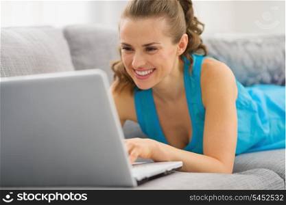 Smiling young woman laying on couch with laptop