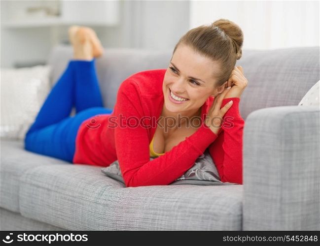 Smiling young woman laying on divan in living room and looking on copy space