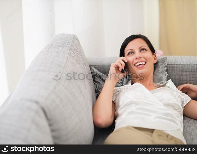 Smiling young woman laying on sofa and speaking mobile phone